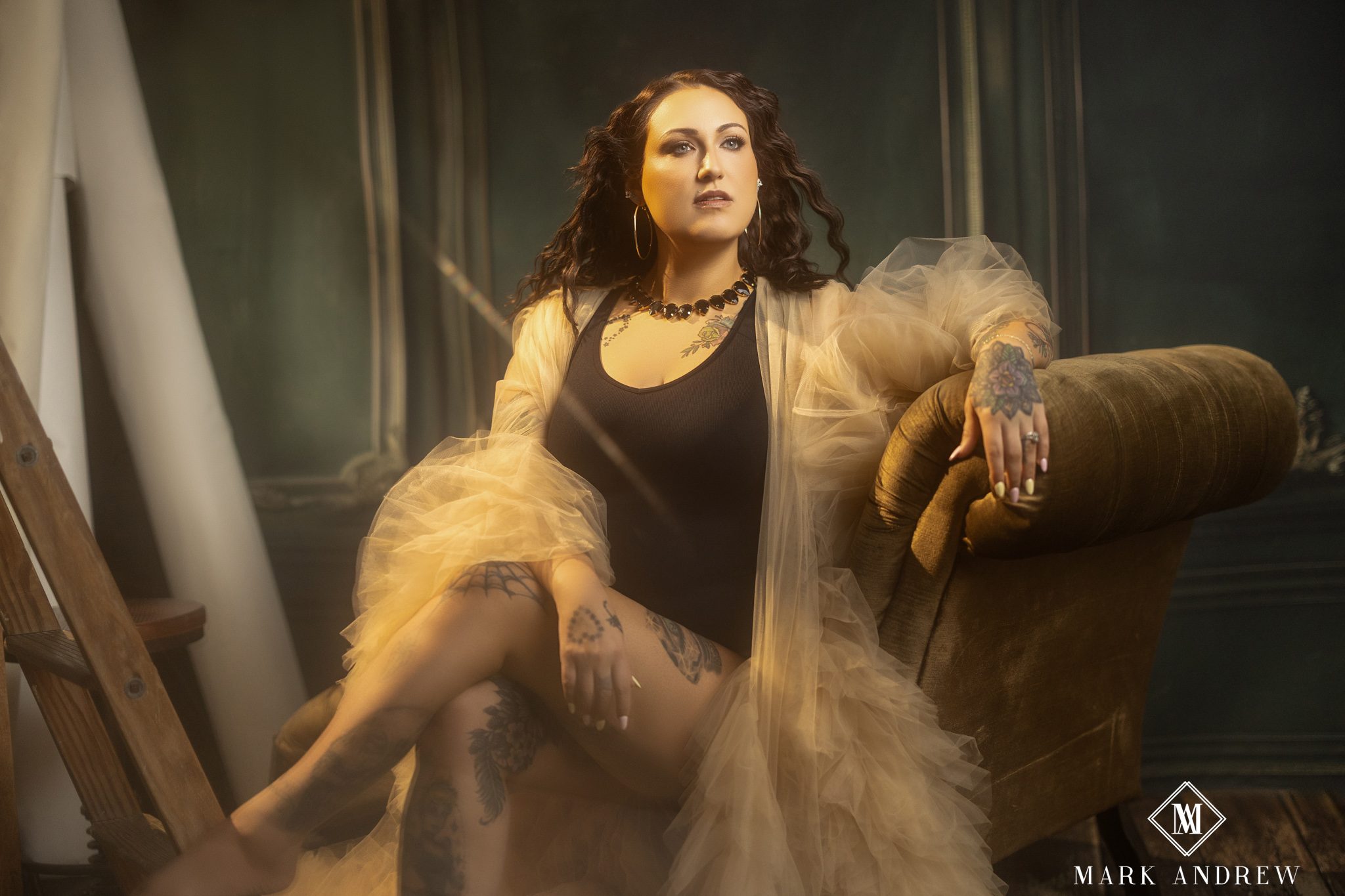 Woman in a black bodysuit and sheer tulle robe seated in a leather chair during a luxury boudoir session near South Bend, Indiana