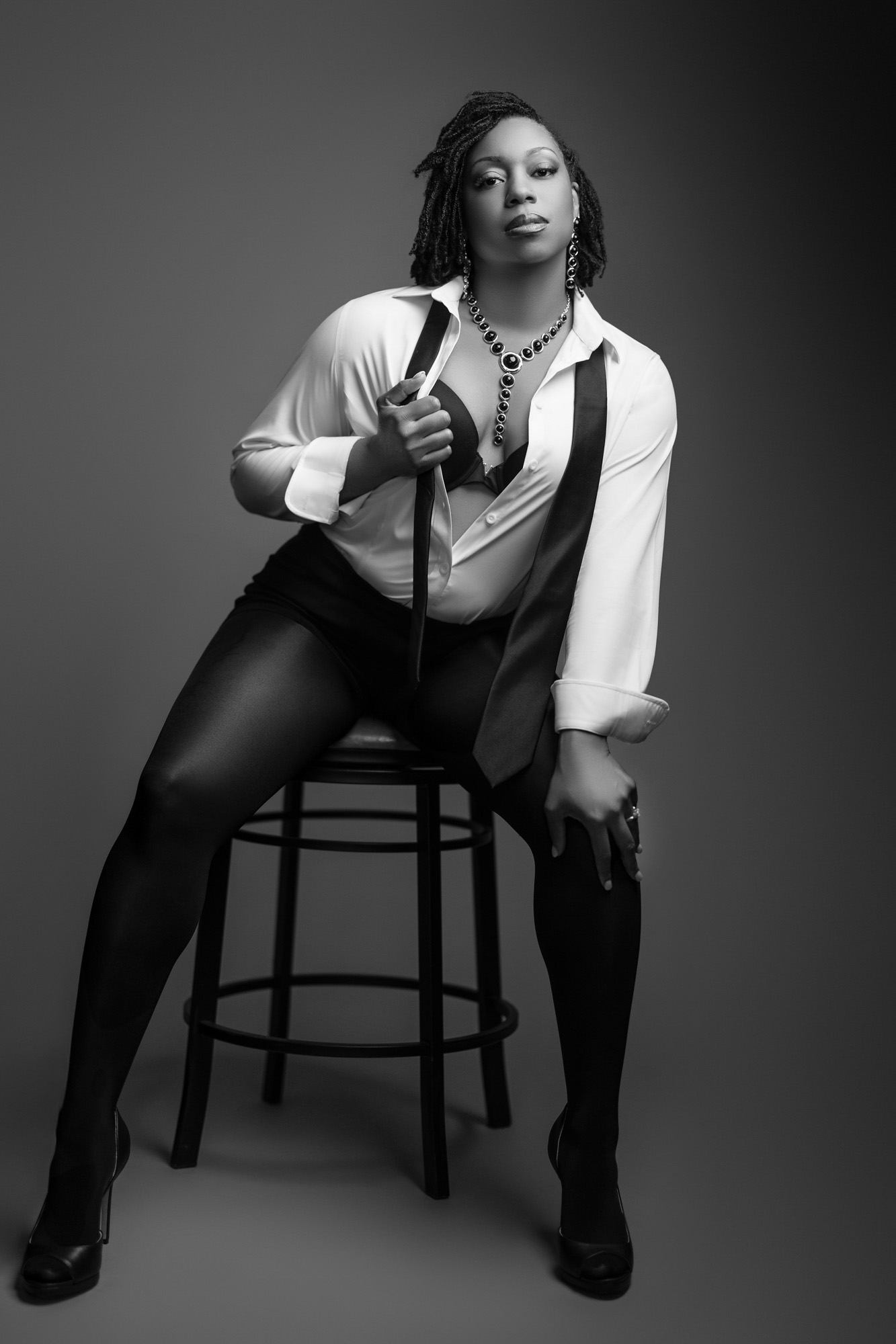 Woman in a white shirt and black tie posed on a barstool during a directed boudoir session near Elkhart, Indiana