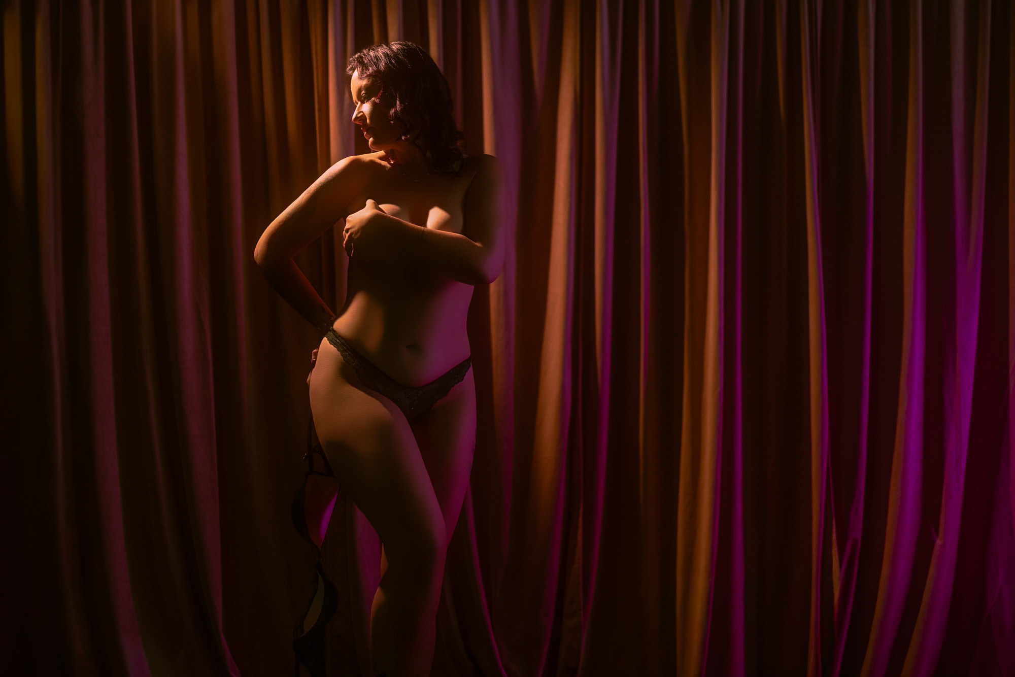 Woman standing in dramatic light against a velvet curtain during a boudoir session in Elkhart, IN
