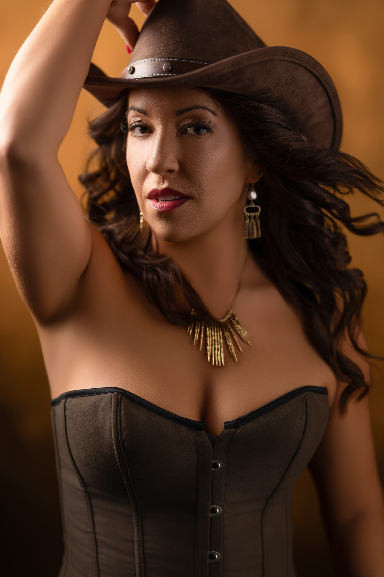 Boudoir client in black corset and cowboy hat in amber light