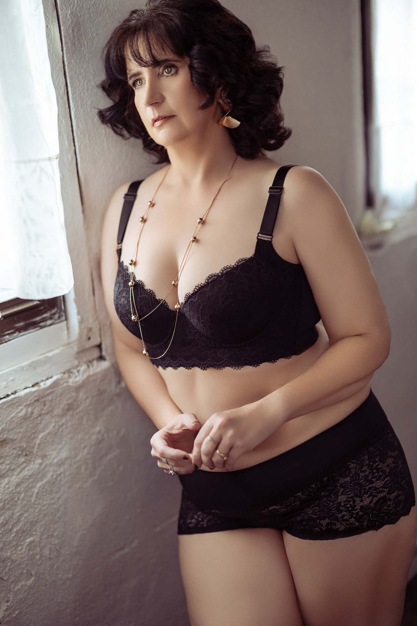 Boudoir client in high-waist black lace shorts in window light