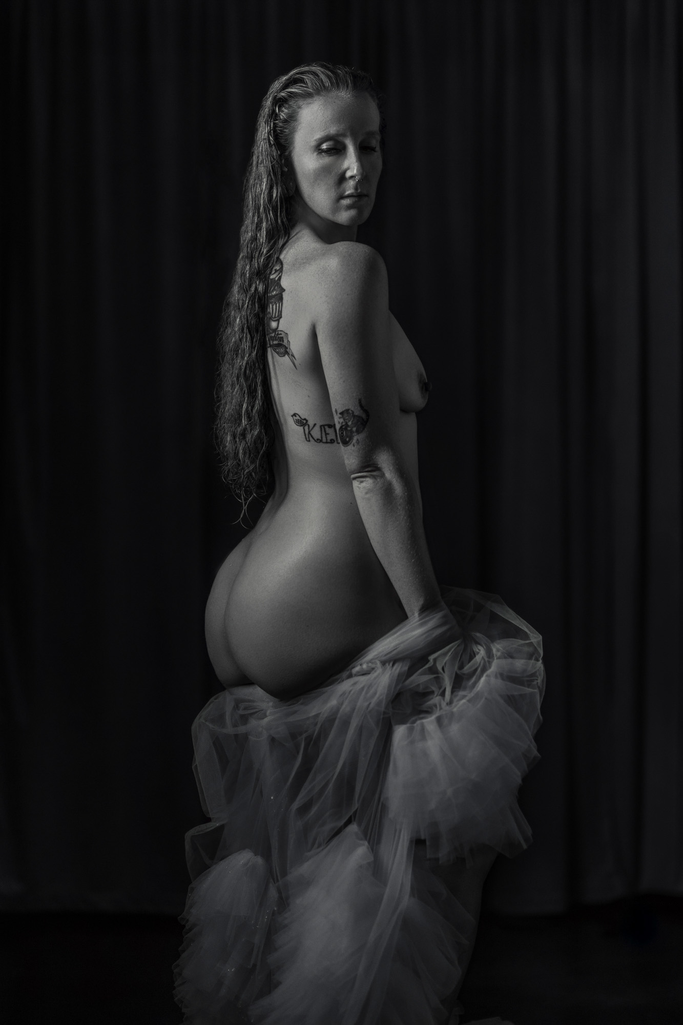 Boudoir client photographed nude from behind in black and white with tulle and side light