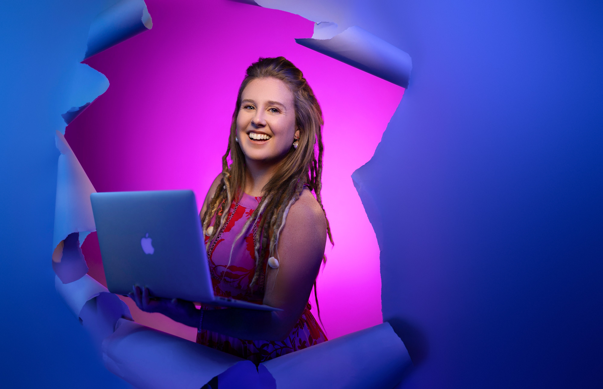 Heidi Spaulding bursting through torn paper with a laptop, lit in magenta and blue — realtor branding photoshoot, Beaufort SC