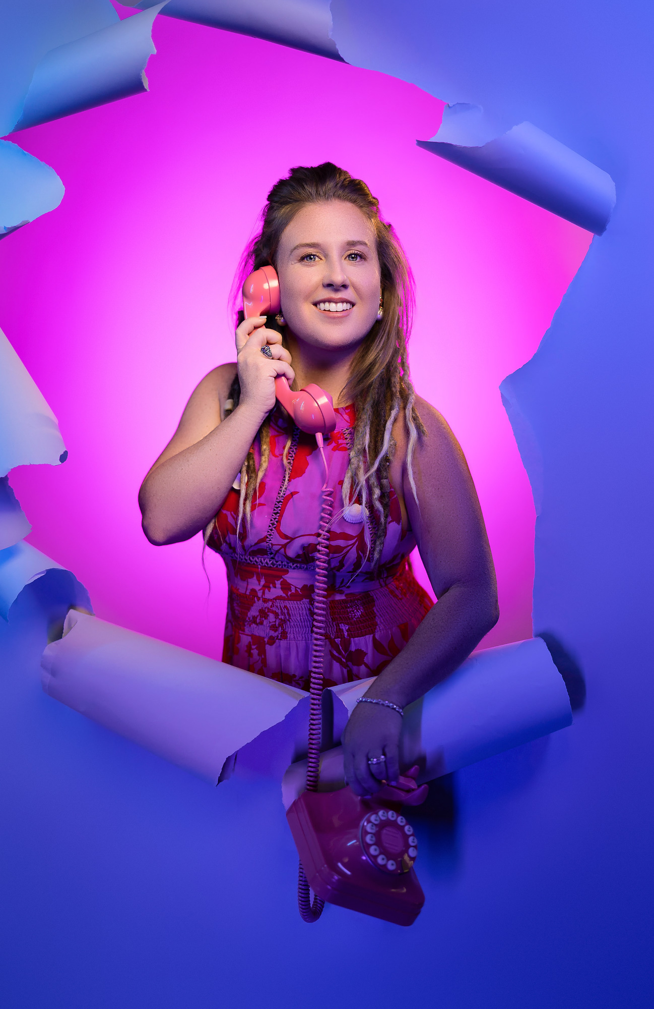 Heidi bursting through torn paper holding a vintage pink rotary phone, lit in magenta and blue — signature realtor branding image, Beaufort SC