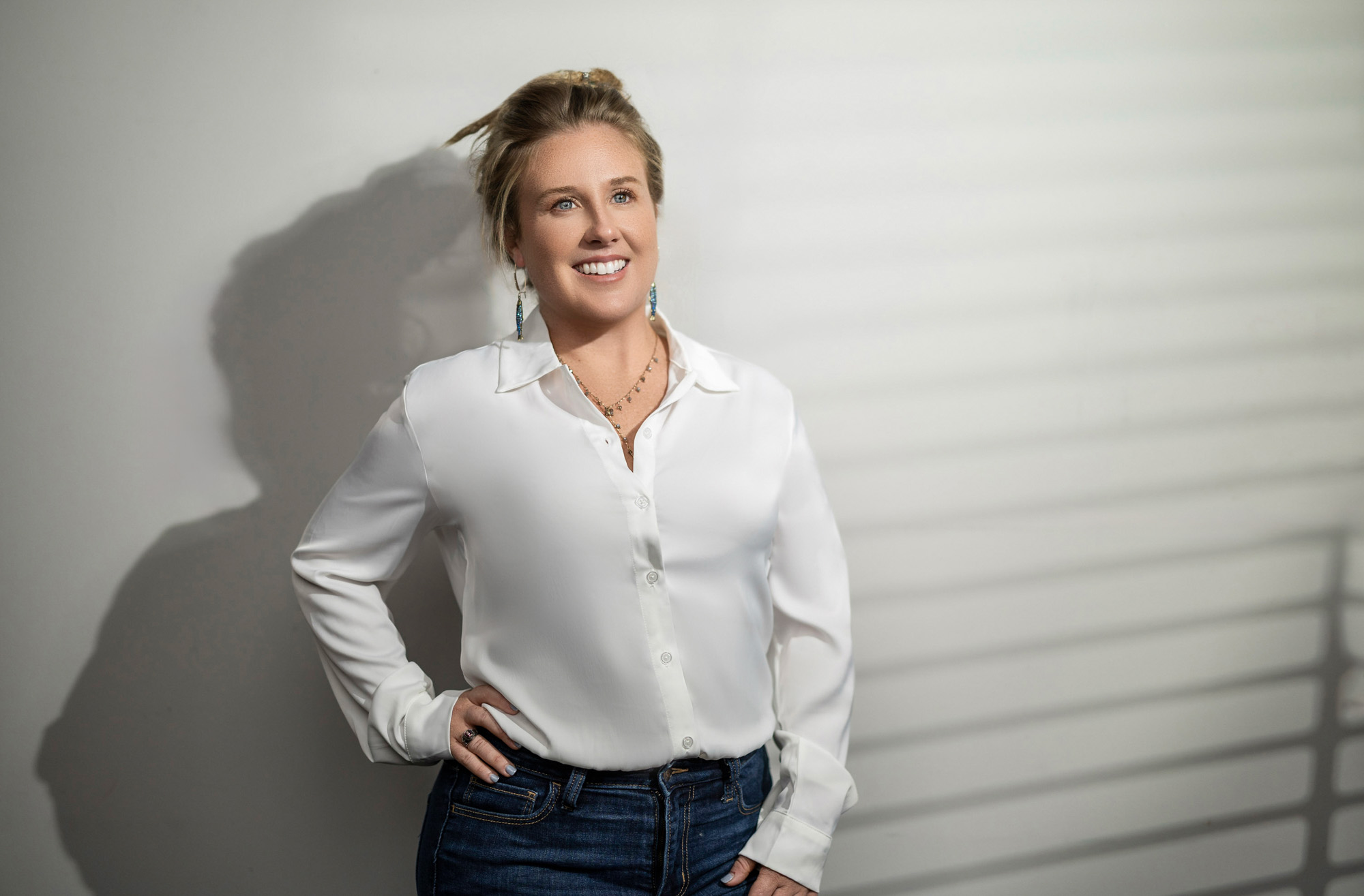 Heidi in a white silk shirt and jeans against a clean light wall — modern realtor branding portrait, Beaufort SC