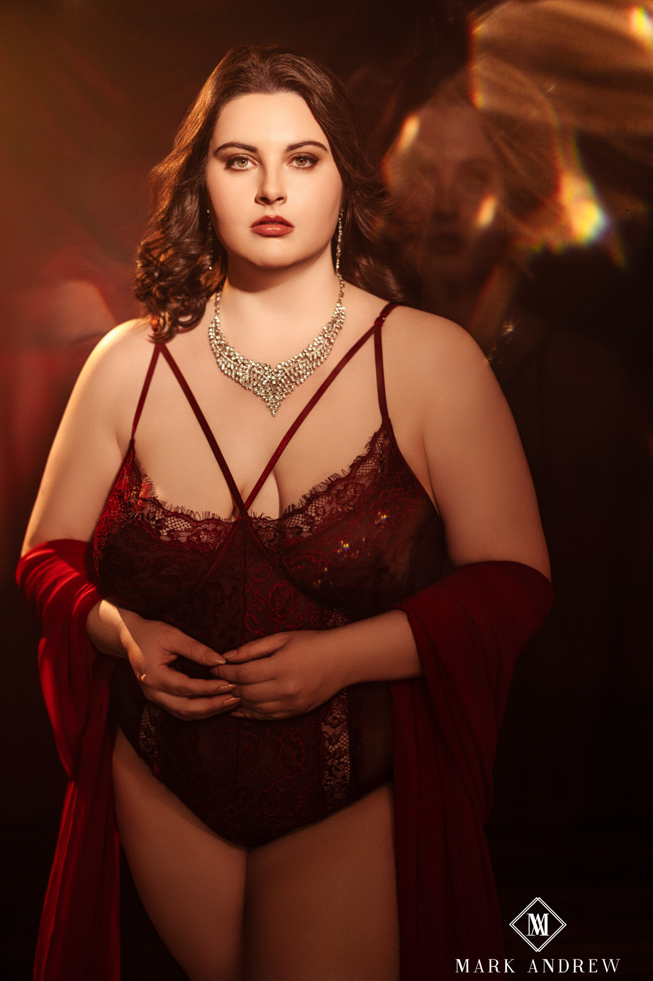 Katherine in a wine-red lace bodysuit with a diamond statement necklace and red drape — luxurious heirloom-quality boudoir portrait