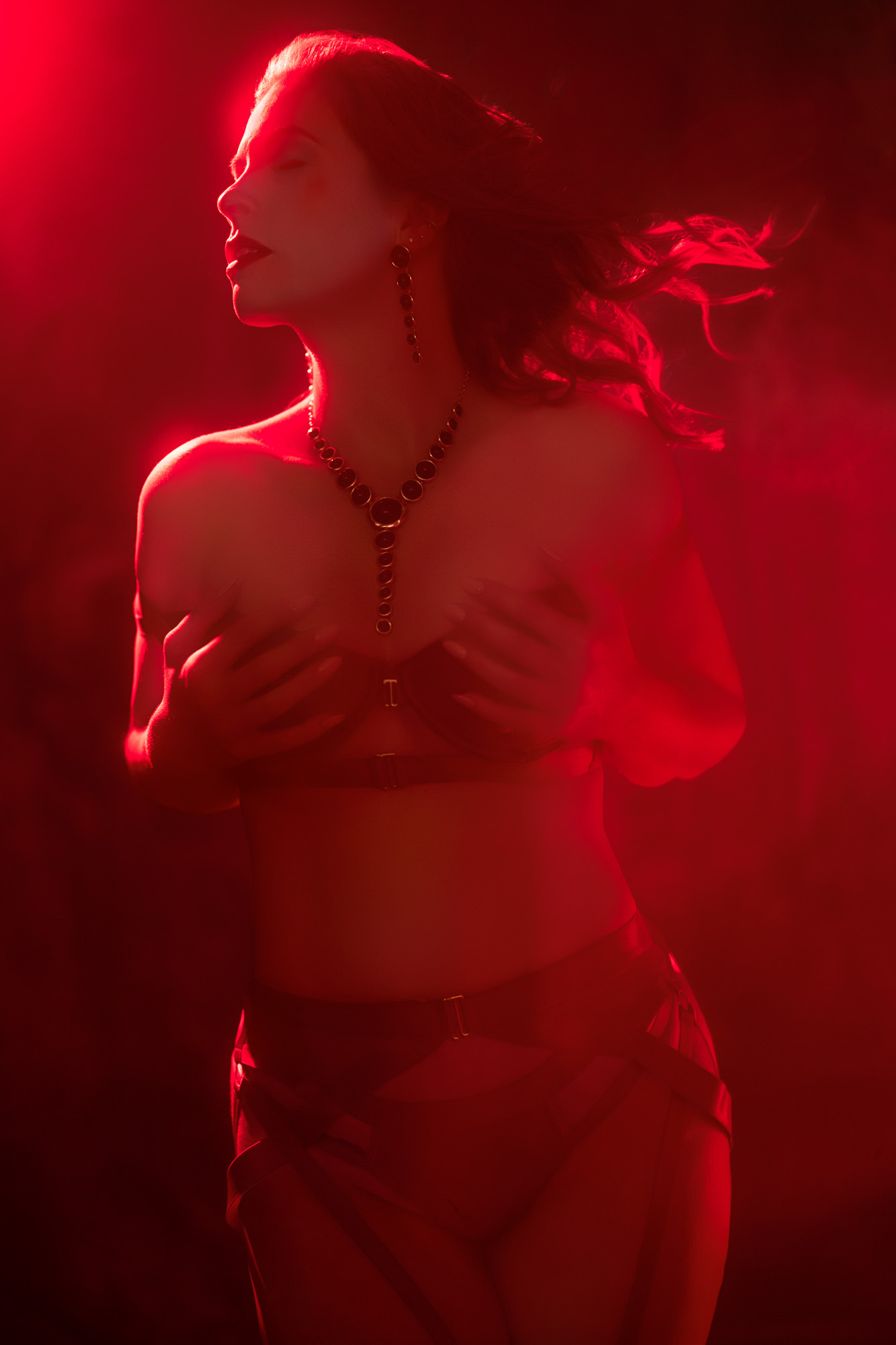 Boudoir client mid-pose with flowing hair under monochromatic red light, captured during a photoshoot